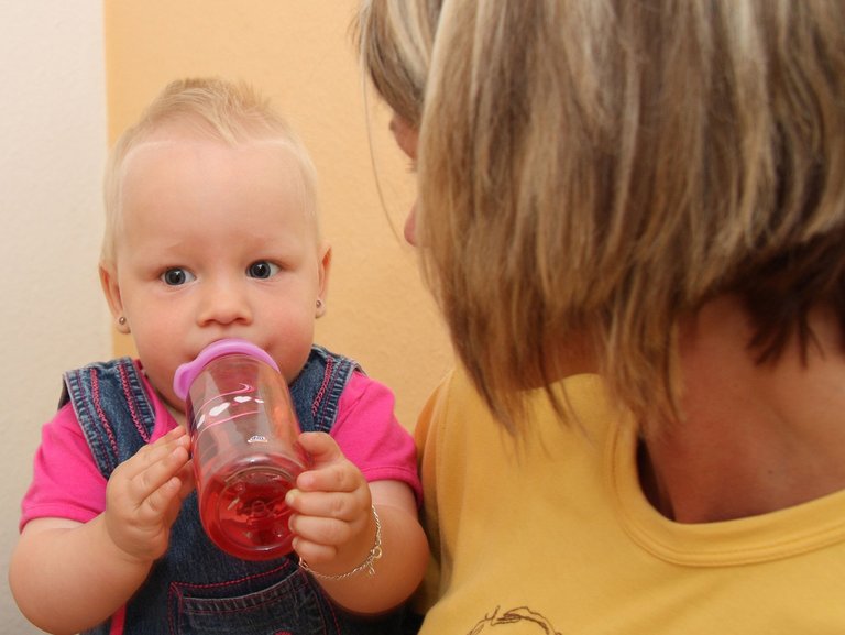 Mutter hält kleines Kind auf dem Arm, während das Kind zufrieden aus einer Flasche trinkt. 