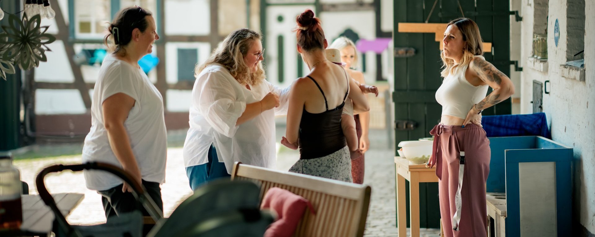 Eine Gruppe Frauen mit einem Baby steht im Innenhof eines Bauernhofes und unterhält sich.