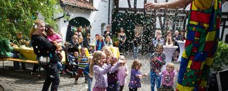 Im Innenhof: Kinder haben Spaß weil ein Clown Konfetti regnen lässt. Eltern schauen freudig zu.