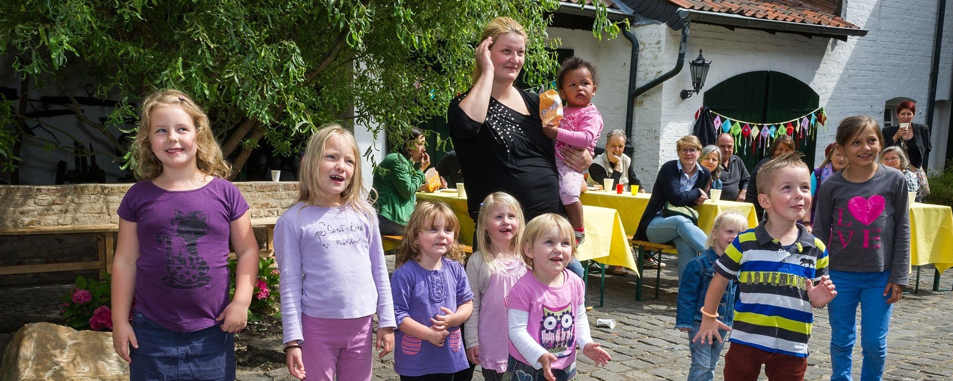 Clownbesuch im Innenhof: kleine Kinder unterschiedlichen Alters schauen gebannt und lächelnd 