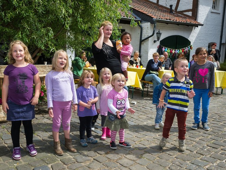 Clownbesuch im Innenhof: kleine Kinder unterschiedlichen Alters schauen gebannt und lächelnd 